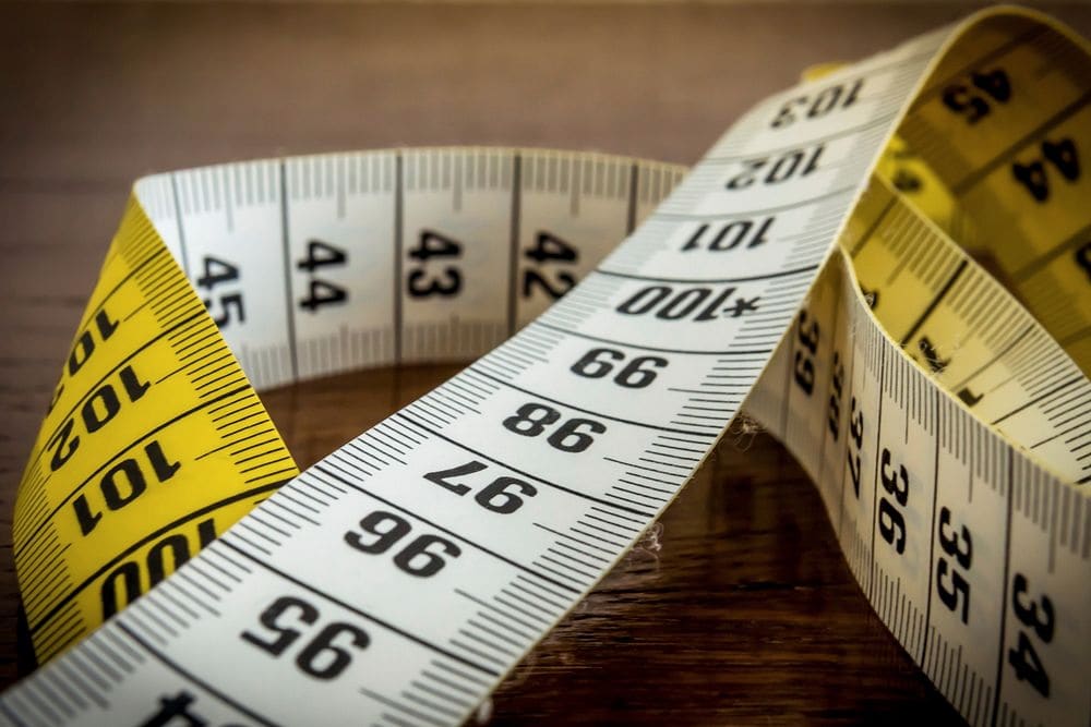 Close view of a white tailor's tape measure curling over a yellow one, the inch and centimeter marks in sharp focus.