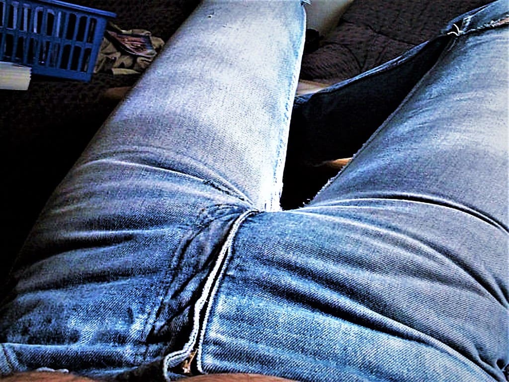 Close view of faded blue jeans creased at the knee, the fabric worn pale along the folds and seams.