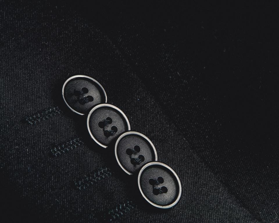 Close view of four dark horn-style buttons on the sleeve of a black wool jacket.