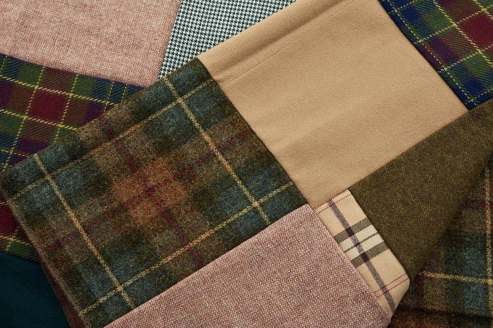Overlapping swatches of wool cloth in green tartan, tan, pink herringbone and small check, laid flat.