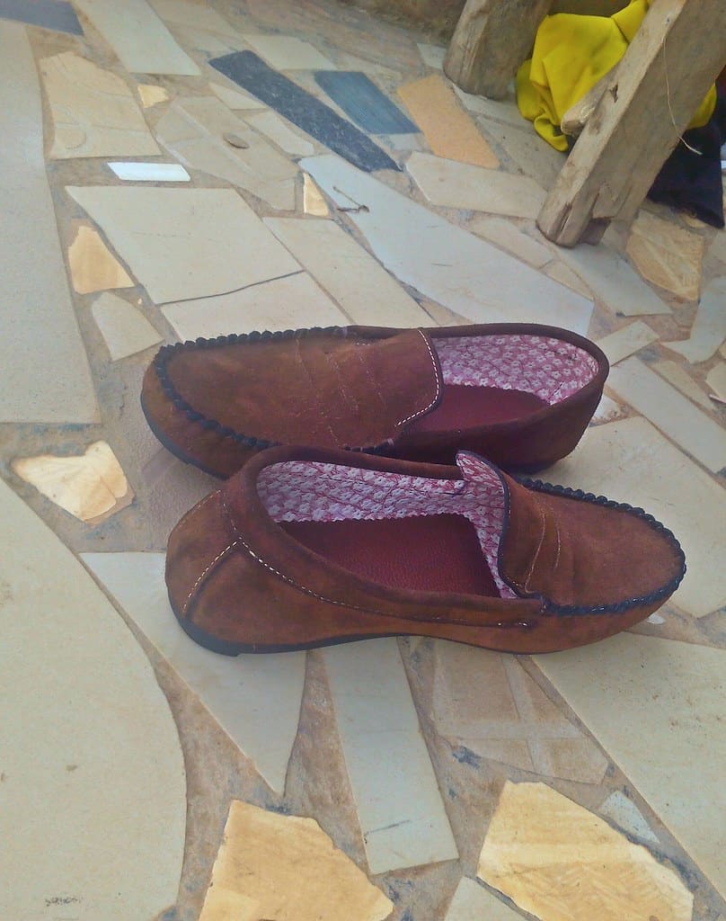 A pair of brown leather slip-on loafers with patterned linings, set on a mosaic stone floor.