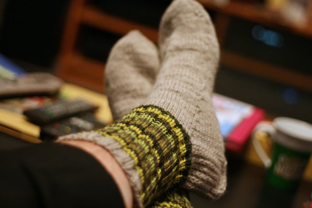 Feet in thick gray wool socks with ribbed green-and-yellow cuffs, propped up indoors.