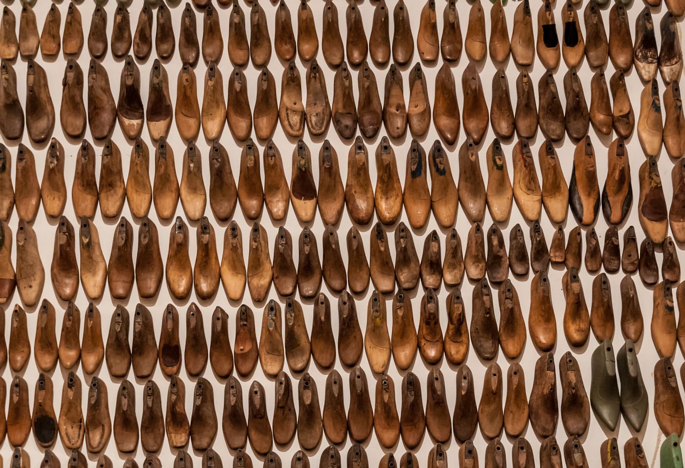 Rows of old wooden shoe forms in light and dark grain, hung close together on a wall.